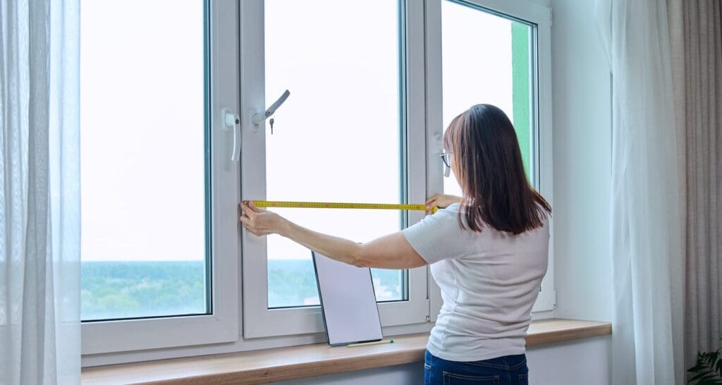 Homeowner measuring windows for replacement.