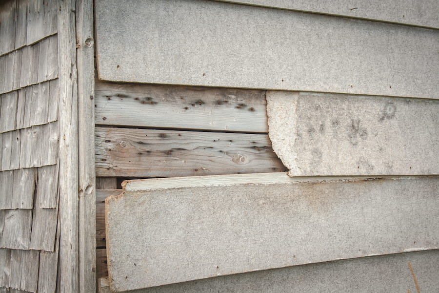 Cracked siding panels with visible gaps allowing moisture intrusion